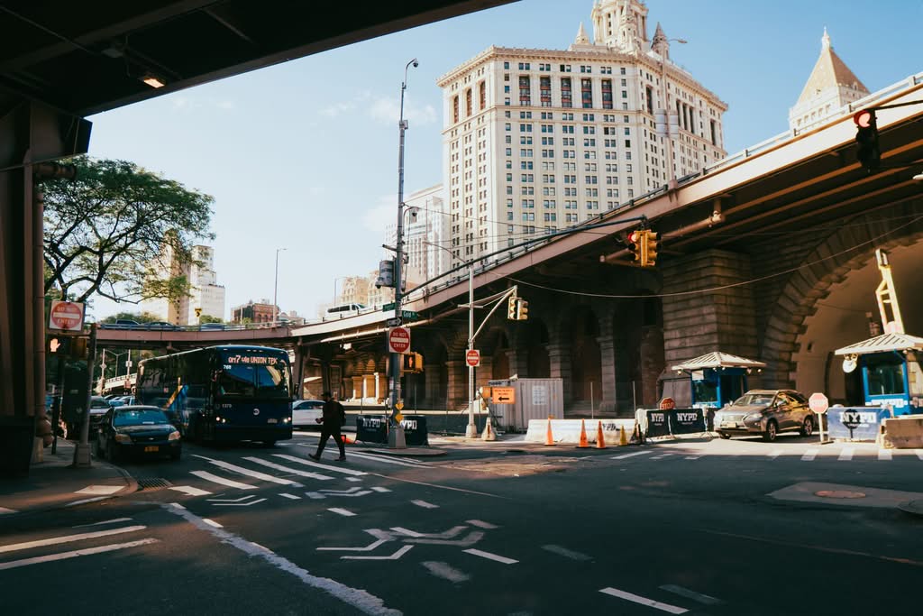 Bustling city street underpass in New York City with vehicles and pedestrians during the day.