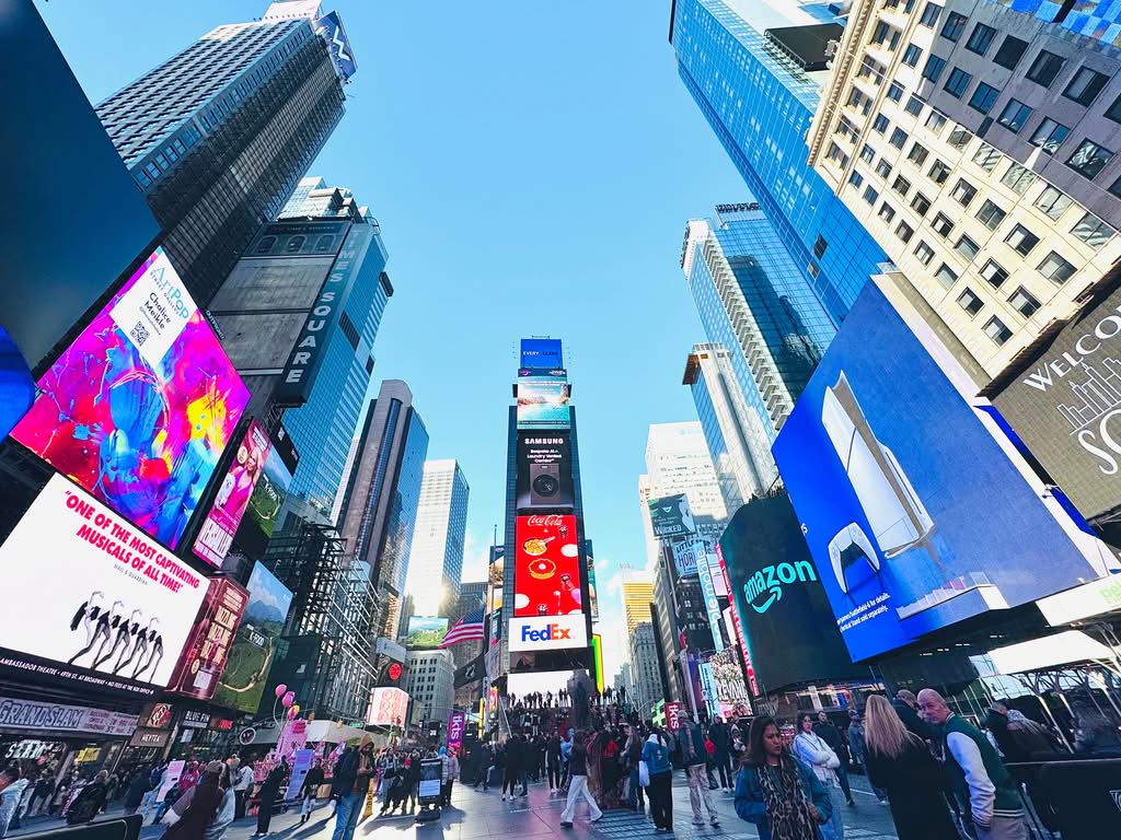 Vibrant daytime view of Times Square, showcasing iconic billboards and bustling crowd in New York City.