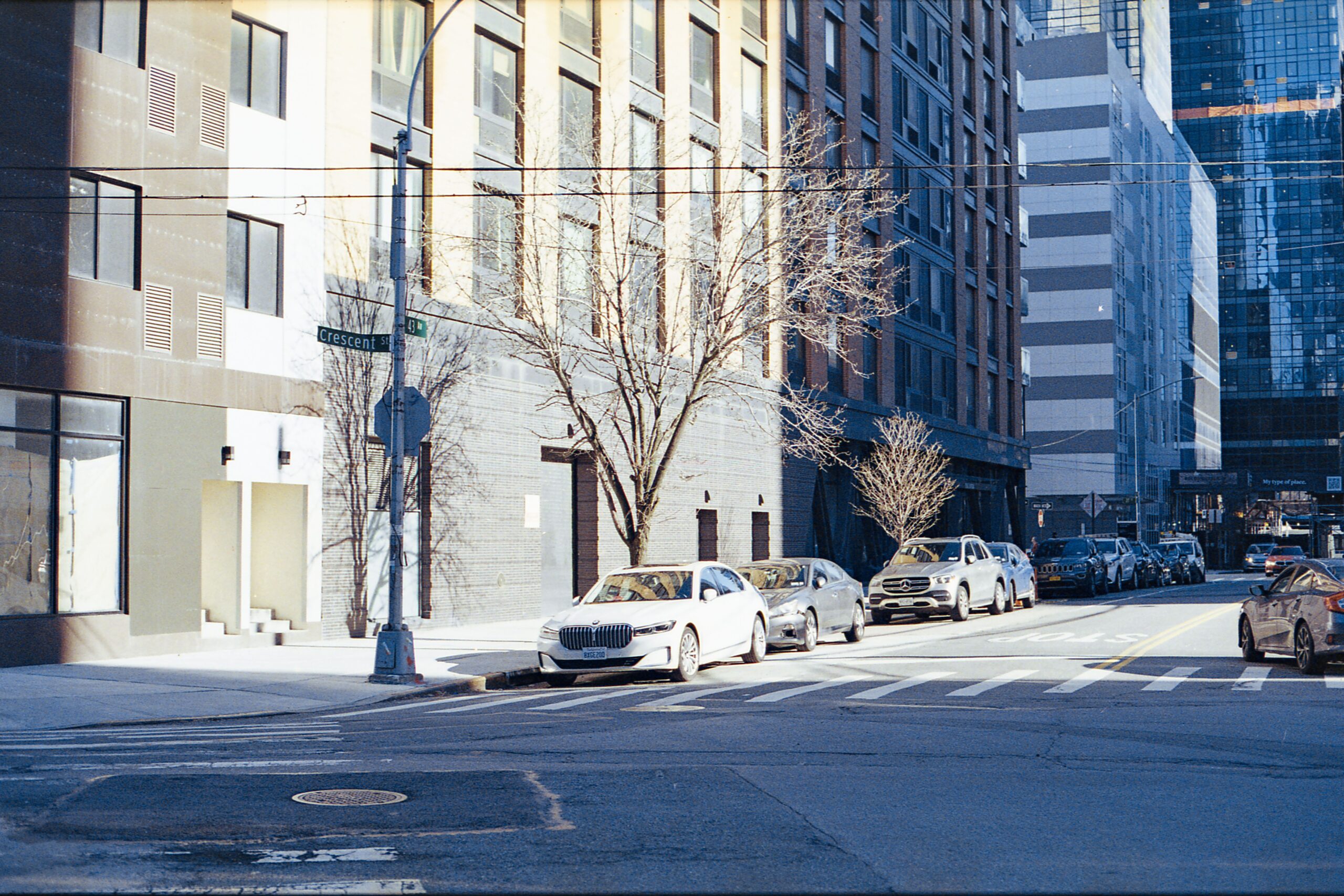 Sunlit street in New York City with parked cars and modern buildings.